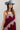 A woman wearing a  maxi dress in deep burgundy with light pink floral lace trim, styled with a dusty blue cowboy hat and holding a blue denim jacket against a plain white studio background.-Lace_Trim_Maxi_Dress_-_Blush_Maroon-FleaStyle