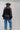 A woman wearing a sheer black lace top in a flowy silhouette, scalloped detailing and an oversized bow and a high ruffled collar, paired with dusty blue cowboy hat and blue jeans, against a plain light gray background-Sheer Lace Tie Neck Blouse - Black