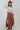 A woman wearing a  flowy maxi skirt featuring cascading asymmetrical tiers, raw-edge detailing and a dramatic side slit and beige sweater paired with a  maroon cowboy hat and brown boots-Asymmetrical_Tiered_Maxi_Skirt_-_Brown-FleaStyle