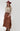 A woman wearing a  flowy maxi skirt featuring cascading asymmetrical tiers, raw-edge detailing and a dramatic side slit and beige sweater paired with a  maroon cowboy hat and brown boots-Asymmetrical_Tiered_Maxi_Skirt_-_Brown-FleaStyle