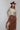 A woman wearing a  flowy maxi skirt featuring cascading asymmetrical tiers, raw-edge detailing and a dramatic side slit and beige sweater is paired with a  maroon cowboy hat and brown boots-Asymmetrical_Tiered_Maxi_Skirt_-_Brown-FleaStyle