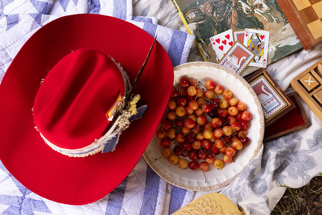Red hat, bowl of berries, playing cards, and vintage map on a checkered fabric background