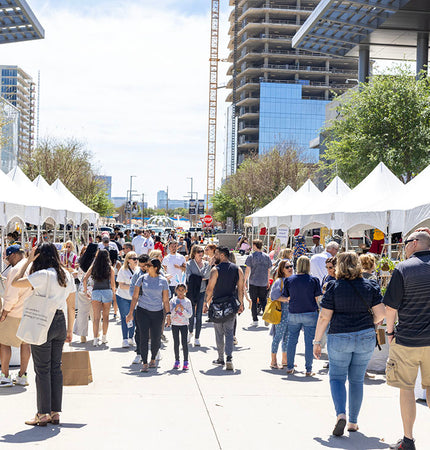 People shopping an outdoor market with vendors set up in white tents 