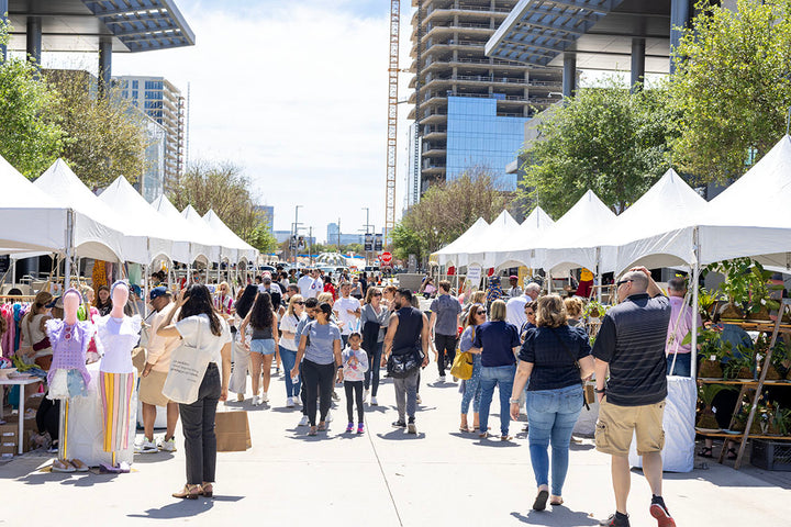 People shopping an outdoor market with vendors set up in white tents 