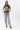 A woman wearing a washed black vintage inspired graphic t-shirt with a "DOLLY" portrait print, paired with light blue jeans and an olive baseball cap with 'Texas' written on it, posed against a solid light gray background-Dolly_Portrait_Graphic_T-Shirt_-_Washed_Black-FleaStyle