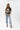 A woman wearing a washed black vintage inspired graphic t-shirt with a "DOLLY" portrait print, paired with light blue jeans and an olive baseball cap with 'Texas' written on it, posed against a solid light gray background-Dolly_Portrait_Graphic_T-Shirt_-_Washed_Black-FleaStyle