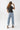A woman wearing a washed black vintage inspired graphic t-shirt with a "DOLLY" portrait print, paired with light blue jeans and an olive baseball cap with 'Texas' written on it, posed against a solid light gray background-Dolly_Portrait_Graphic_T-Shirt_-_Washed_Black-FleaStyle