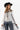 A woman wearing a western-style outfit featuring a white long-sleeve button-up shirt, a sheer black mesh overlay, featuring a relaxed, sleeveless fit and a flowy tulle hem, blue jeans, a black cowboy hat, and black ankle boots, against a plain white studio background-Sleeveless_Sheer_Mesh_Overlay_-_Black-FleaStyle
