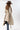 A smiling woman wearing a brown cowboy hat, a beige sleeveless vest with robe tie and oversized faux-fur collar, jeans and a white long-sleeve top, photographed against a clean white studio background-Fur Trimmed Sleeveless Duster Vest - Taupe