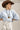 A woman wearing a light blue knit sweater, a brown straw wide-brim hat, a long black beaded necklace with a gold pendant, and a white floral skirt-Short_Sleeve_Mock_Neck_Sweater_-_Dusty_Blue-FleaStyle