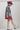 A woman models a western-style outfit featuring a playful Western Embroidered Patch Blazer with colorful embroidered patches, a berry cowboy hat, a striped dress, and silver cowboy boots --Western_Embroidered_Patch_Blazer-FleaStyle