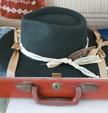Green fedora hat with decorative ribbons on a vintage suitcase