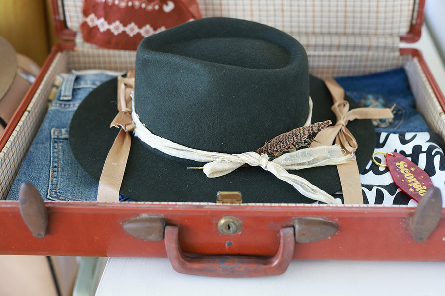Green fedora hat with decorative ribbons on a vintage suitcase