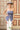 A woman wearing a strapless blue corset-style top with gold-tone buckle clasps, a long satin maxi skirt with a colorful printed  horse design, paired with a beige cowboy hat and dark blue boots, against studio background-Western_Buckle_Strapless_Top_-_Dusty_Blue-FleaStyle