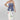 A woman wearing a strapless blue corset-style top with gold-tone buckle clasps, a long satin maxi skirt with a colorful printed  horse design, paired with a beige cowboy hat and dark blue boots, against studio background-Western_Buckle_Strapless_Top_-_Dusty_Blue-FleaStyle