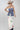 A woman wearing a strapless blue corset-style top with gold-tone buckle clasps, a long satin maxi skirt with a colorful printed  horse design, paired with a beige cowboy hat and dark blue boots, against studio background-Western_Buckle_Strapless_Top_-_Dusty_Blue-FleaStyle