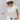 A woman wearing a cream-colored drawstring top with an easy relaxed fit ,adjustable side ruching and ties, a matching cream wide-brim hat, layered gold necklaces, and a white skirt with colorful horse prints, posing against a light gray studio background-Ruched_Drawstring_Top_-_Ivory-FleaStyle