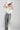 A woman wearing a high-waisted pant with allover snakeskin print with shimmering sequin detailing and an easy straight-leg silhouette, styled with a cream ruched top, an  ivory cowboy hat and gold jewelry against a light gray studio background--Sequin_Snakeskin_Print_Wide_Leg_Pants-FleaStyle