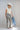 A woman wearing a high-waisted pant with allover snakeskin print with shimmering sequin detailing and an easy straight-leg silhouette, styled with a cream ruched top, an  ivory cowboy hat and gold jewelry against a light gray studio background--Sequin_Snakeskin_Print_Wide_Leg_Pants-FleaStyle