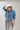 A woman wearing a light blue cropped denim relaxed denim shirt-jacket, an ivory cowboy hat, and high-waisted pant with allover snakeskin print and shimmering sequins--Cropped_Denim_Shacket-FleaStyle