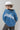 A model wearing a  cropped denim jacket featuring an oversized dolman-sleeve silhouette with unexpected asymmetrical lace detailing , paired with leopard-print pants, an ivory cowboy hat, and shiny silver cowboy boots, photographed against a light gray studio background--Lace_Trim_Dolman_Denim_Jacket-FleaStyle