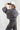 A woman wearing a charcoal gray oversized button-down shirt with a relaxed fit, voluminous sleeves and a soft bubble hem, leopard-print wide-leg jeans, silver cowboy boots, and a Texas trucker hat --Bubble_Sleeve_Button_Down_Top_-_Charcoal_Gray-FleaStyle