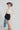 A woman wearing a cream long-sleeve dramatic blouse with black polka dots and a high gathered neckline and adjustable neck tie, paired with a black mini skort  with a flattering high-rise fit with a flowy silhouette and a gray cowboy hat, against a light gray studio background--Suede Pleated Skort - Black
