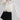 A woman wearing a cream long-sleeve dramatic blouse with black polka dots and a high gathered neckline and adjustable neck tie, paired with a black mini skort and a gray cowboy hat, against a light gray studio background--Flowy_Polka_Dot_Tie_Blouse_-_Ivory-FleaStyle  