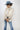 A woman wearing a cream blouse with dark polka dots, mid-rise cropped jeans with a silhouette fit through the hips and thighs and easy kick flare, and a dusty  blue cowboy hat-Mid-Rise_Cropped_Bootcut_Jeans-FleaStyle.
