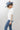 A woman wearing a white short-sleeve crop top with a lace sheer underlay in a delicate floral pattern, with fitted silhouette and thumb holes, blue jeans, and a dusty blue cowboy hat -Lace_Mock_Neck_Sheer_Underlay_-_Beige-FleaStyle