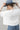 A woman wearing a white short-sleeve crop top with a lace sheer underlay in a delicate floral pattern, with fitted silhouette and thumb holes, blue jeans, and a dusty blue cowboy hat -Lace_Mock_Neck_Sheer_Underlay_-_Beige-FleaStyle
