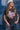 Woman in a trucker hat, Choosin' Texas Graphic T-Shirt - Pink- denim shorts and cowboy boots in front of a denim patchwork background-Fleastyle