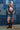 Woman in a trucker hat, Choosin' Texas Graphic T-Shirt - Pink- denim shorts and cowboy boots in front of a denim patchwork background-Fleastyle