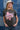 Woman in a trucker hat, Choosin' Texas Graphic T-Shirt - Pink- denim shorts and cowboy boots in front of a denim patchwork background-Fleastyle