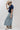 A woman wearing a classic mock neckline knit sweater, easy short sleeves and a bold ivory star, a beige cowboy hat, light-wash denim pants, and brown cowboy boots with blue star embroidery, sitting on a white studio floor--Star_Short-Sleeve_Knit_Sweater_-_Navy-FleaStyle