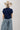 A woman wearing a classic mock neckline knit sweater, easy short sleeves and a bold ivory star, a beige cowboy hat, light-wash denim pants, and brown cowboy boots with blue star embroidery, sitting on a white studio floor--Star_Short-Sleeve_Knit_Sweater_-_Navy-FleaStyle