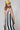 A woman modeling a sleeveless midi dress with bold black and white vertical stripes, paired with a yellow trucker hat and patterned shoes-Vertical Stripe Midi Dress - Black/Ivory