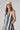 A woman modeling a sleeveless midi dress with bold black and white vertical stripes, paired with a yellow trucker hat and patterned shoes-Vertical Stripe Midi Dress - Black/Ivory