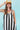 A woman modeling a sleeveless midi dress with bold black and white vertical stripes, paired with a yellow trucker hat and patterned shoes-Vertical Stripe Midi Dress - Black/Ivory