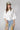 A woman wearing a white oversized button-down shirt with rolled sleeves and an olive baseball cap that reads 'Laguna BEACH' in white text-Back Pleat Button Down Blouse - Off-White