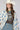 A woman wearing a bohemian-style Crochet-Duster-Cardigan-Ivory_Blue-FleaStyle, a brown  top, wide-leg denim jeans, an ivory white cowboy hat, and lace-up heeled sandals-FleaStyle