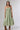 A woman wearing a light sage green strapless midi dress with a gathered sweetheart neckline, paired with brown cowboy boots, an olive  trucker hat, and a gold necklace-FleaStyle