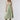 A woman wearing a light sage green strapless midi dress with a gathered sweetheart neckline, paired with brown cowboy boots, an olive  trucker hat, and a gold necklace-FleaStyle