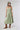 A woman wearing a light sage green strapless midi dress with a gathered sweetheart neckline, paired with brown cowboy boots, an olive  trucker hat, and a gold necklace-FleaStyle
