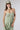 A woman wearing a light sage green strapless midi dress with a gathered sweetheart neckline, paired with brown cowboy boots, an olive  trucker hat, and a gold necklace-FleaStyle