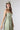 A woman wearing a light sage green strapless midi dress with a gathered sweetheart neckline, paired with brown cowboy boots, an olive  trucker hat, and a gold necklace-FleaStyle