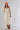 A woman wearing a sleeveless, cream-colored midi dress with a smocked bodice and gathered skirt, styled with brown cowboy boots and an orange 'Laguna Beach' baseball cap -Pintuck Detail Midi Dress - Khaki