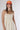 A woman wearing a sleeveless, cream-colored midi dress with a smocked bodice and gathered skirt, styled with brown cowboy boots and an orange 'Laguna Beach' baseball cap -Pintuck Detail Midi Dress - Khaki