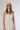 A woman wearing a sleeveless, cream-colored midi dress with a smocked bodice and gathered skirt, styled with brown cowboy boots and an orange 'Laguna Beach' baseball cap -Pintuck Detail Midi Dress - Khaki