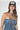 A woman wearing a strapless tiered denim maxi dress in a medium blue wash, paired with a brown baseball cap that reads 'Laguna BEACH' and layered gold necklaces-Fleastyle